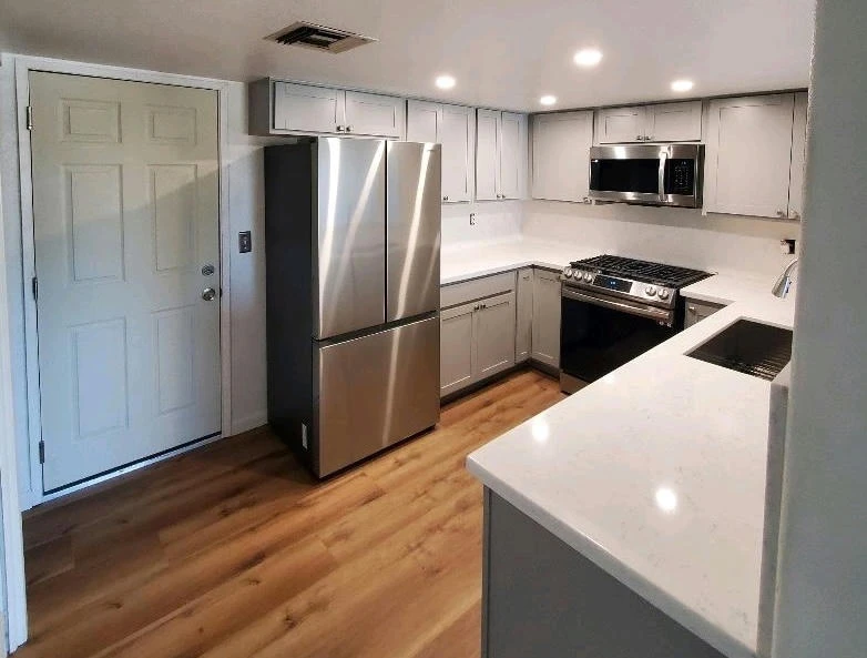 Newly remodeled kitchen with light gray cabinets, white quartz countertops, stainless steel appliances, and wood floor